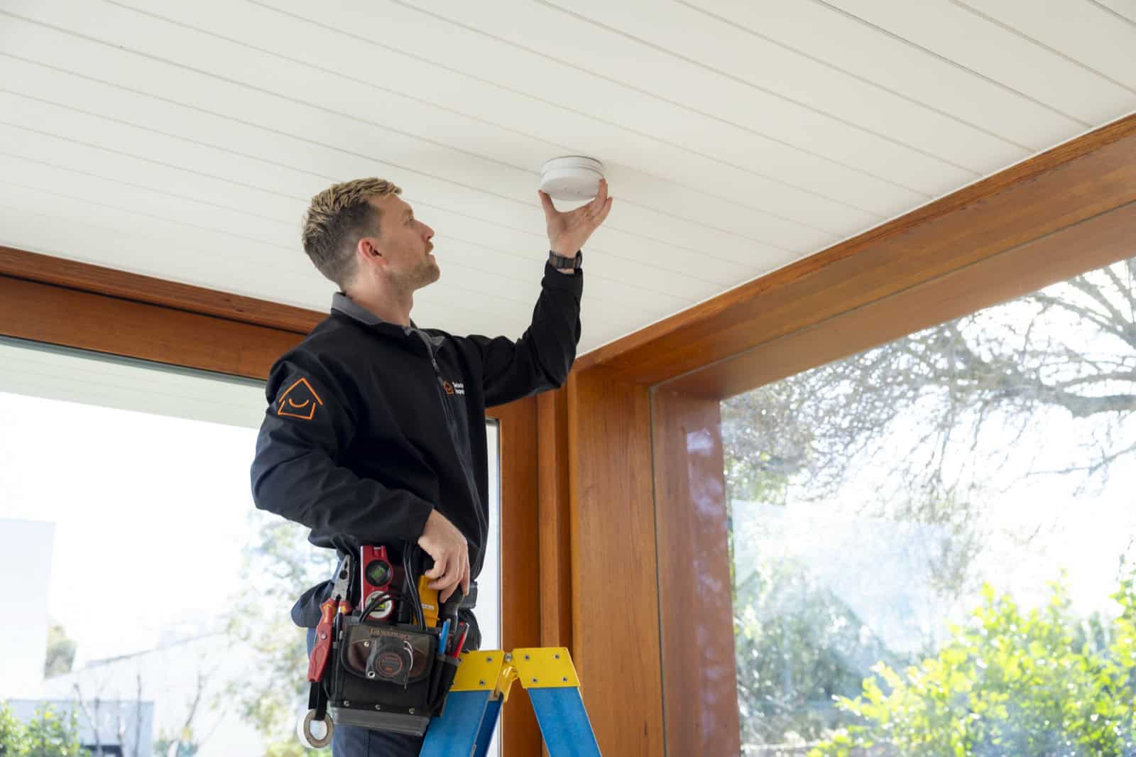 A Detector Inspector technician installing a photoelectric smoke alarm on a ceiling